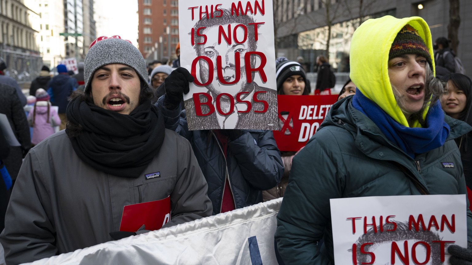 A group of federal workers protesting on the streets of New York. They hold signs with Elon Musk's face that read "This man is not our boss."