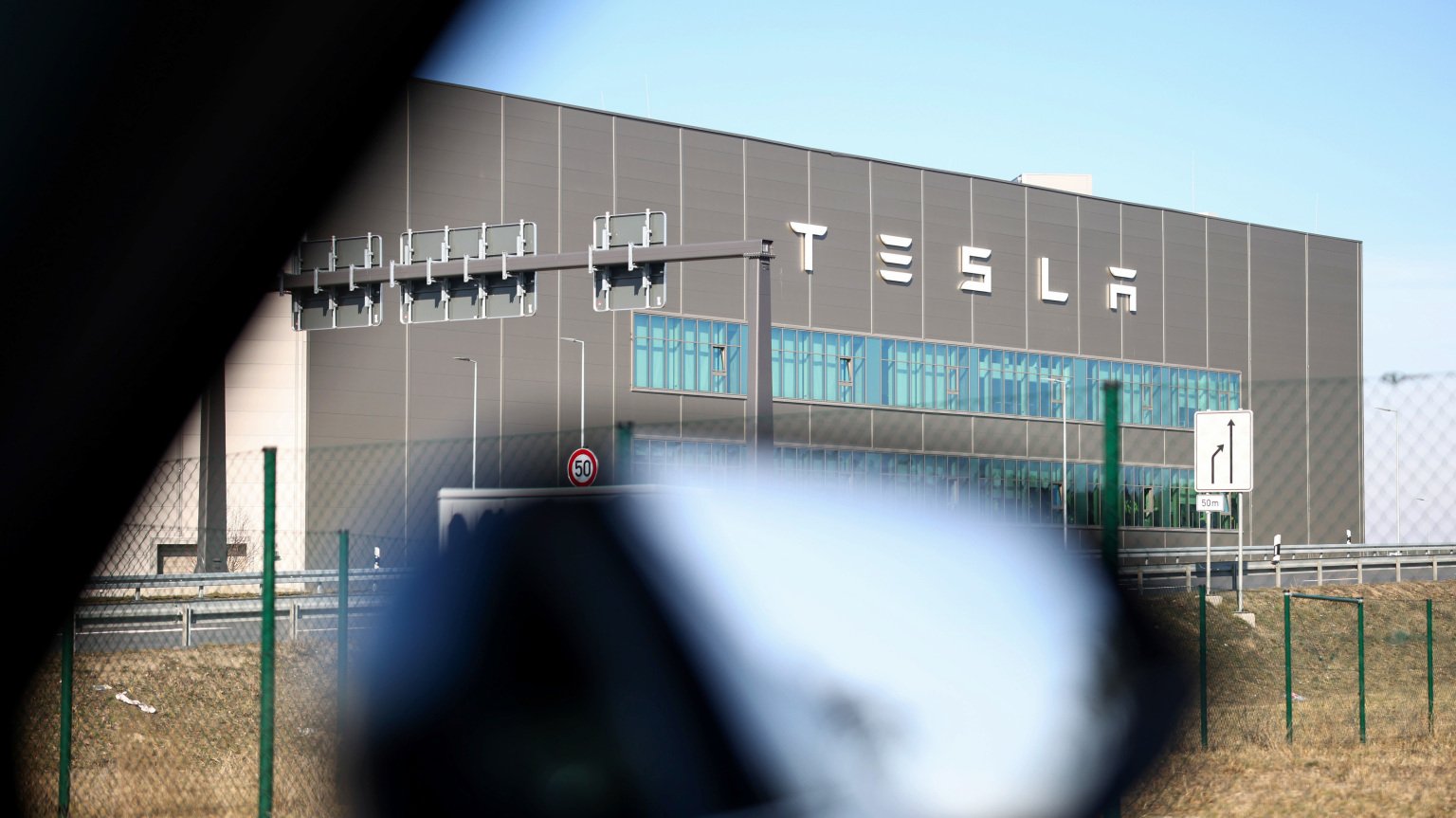A photo of the outside of a Tesla factory framed through the window of a car. 