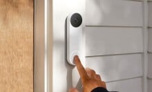 an index finger rings the google nest doorbell that's attached to a house next to the front door