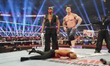 The Rock and John Cena stand over Cody Rhodes at WWE Elimination Chamber