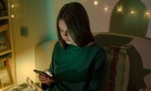 Sitting in her bedroom, a teen girl looks down at her phone.
