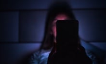 A woman stares at her phone in the dark.