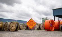A group of large spools of orange and black fiber optic cables on a construction site. An orange sign reads, "Fiber construction ahead."