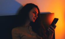 young woman sitting in a dimly lit room, browsing her smartphone