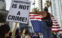 A group of protestors wave an upside down American flag and a sign that reads "protesting is not a crime!"