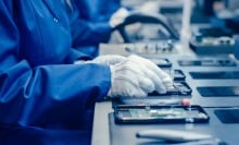 Factory Worker in Blue Work Coat and Protective Glasses Assembling Smartphones with Screwdriver
