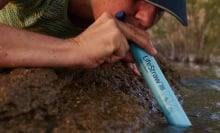 woman sipping from lifestraw inserted in river