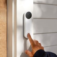 an index finger rings the google nest doorbell that's attached to a house next to the front door