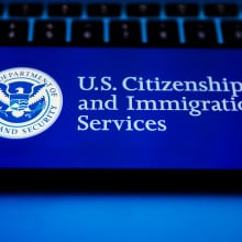 A cell phone displaying the US citizenship and immigration services logo rests on a keyboard.