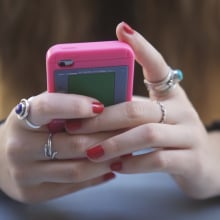teenage girl with red nail polish holding iphone with pink case