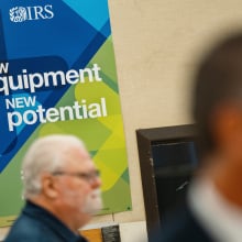 An IRS employee sits in front of a sign that reads "new equipment, new potential."