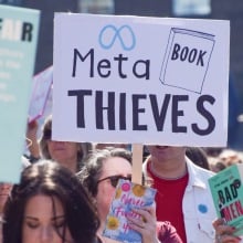 A protester holds a 'Meta book thieves' placard in King's Cross during the march to Meta offices
