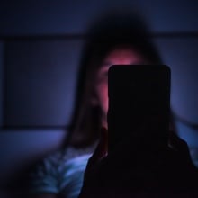 A woman stares at her phone in the dark.