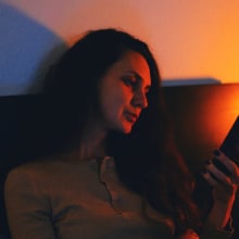 young woman sitting in a dimly lit room, browsing her smartphone