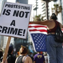 A group of protestors wave an upside down American flag and a sign that reads "protesting is not a crime!"