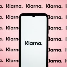 A phone displays the Klarna logo in front of a pink background.