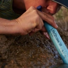 woman sipping from lifestraw inserted in river