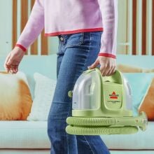 woman carrying bissell little green mini through living room