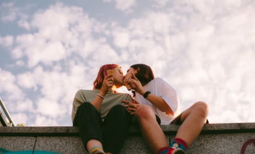 Lesbian couple kissing while sitting on a concrete wall outside