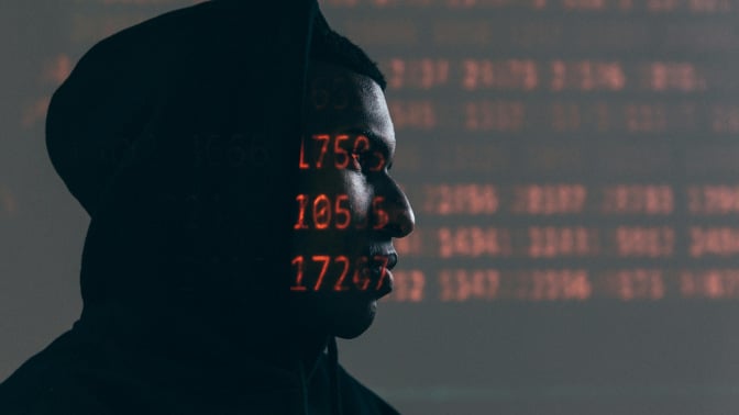 sketchy computer hacker in a hoodie with computer code projected on face