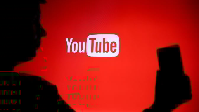 The YouTube logo with a shadowed outline of a person using a phone in the foreground.