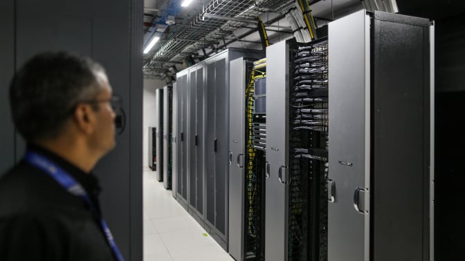 A man stands looking at a bank of AI data processors.
