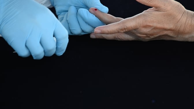 gloved hands pricking a finger for blood