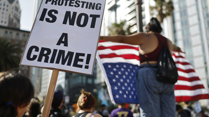 A group of protestors wave an upside down American flag and a sign that reads "protesting is not a crime!"