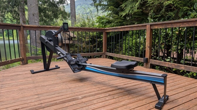 the merach r50 rowing machine on a poorly stained deck in front of a lake