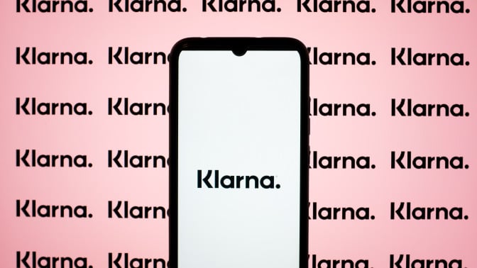 A phone displays the Klarna logo in front of a pink background.