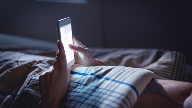 woman lying in bed and looking at glowing phone screen