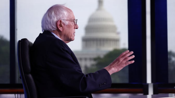 bernie sanders sitting at a desk with the capitol building in the background