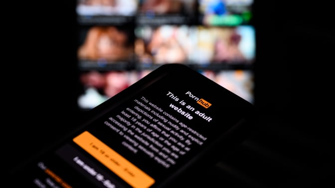pornhub age restriction page in front of blurred stills of porn videos