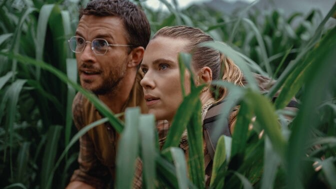 Jonathan Bailey and Scarlett Johansson stand in tall grass in "Jurassic World Rebirth."