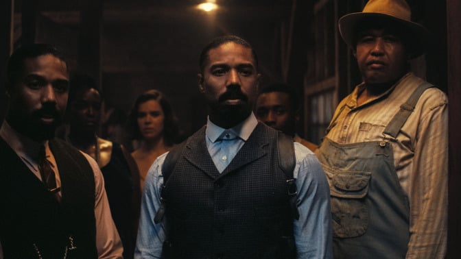 A still from "Sinner", Michael B. Jordan, playing twins Smoke and Stack, and Omar Benson Miller as Cornbread, stand in a dimly lit doorway and look out into the night with wary expressions. 