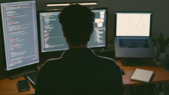 back of engineer's head sitting at multiple computer monitors