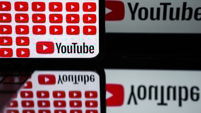 Phone and laptop screens display the YouTube logo, which is reflected in a mirror below them. 