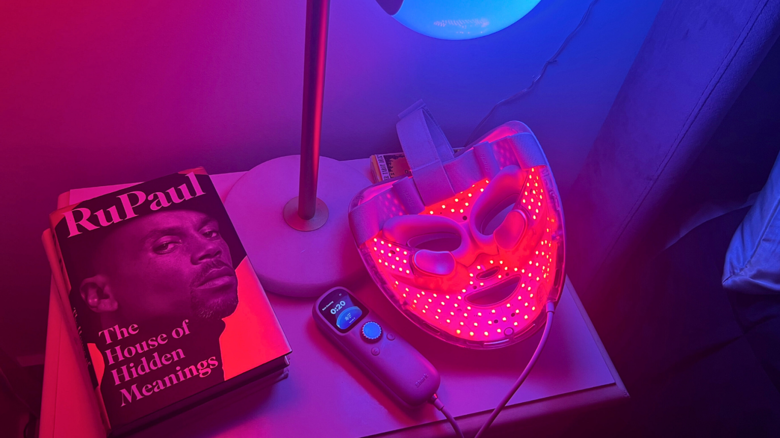 Shark red light face mask, lamp, and book on nightstand