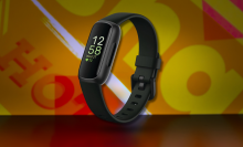 A close-up of the Fitbit Inspire 3 in black, with its screen illuminated, against a colorful, patterned background.