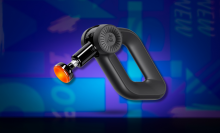 A black Bob and Brad D6 Pro massage gun with an orange, glowing heated massage head is angled to the left against an abstract blue and purple background.