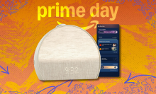 A photo composite of the Hatch Restore 3 alarm clock in a putty color, shown against a stylized orange and yellow Prime Day background. A smartphone displaying the Hatch app is visible next to the clock.
