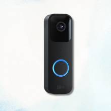 Black Blink video doorbell with a glowing blue ring on a light blue and white background.