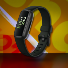A close-up of the Fitbit Inspire 3 in black, with its screen illuminated, against a colorful, patterned background.
