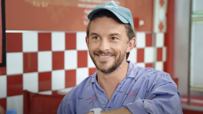 A man wearing a hat while smiling at someone offscreen.