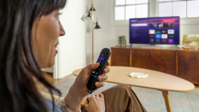 woman speaking into Roku voice remote and watching tv through Roku Streaming Stick Plus